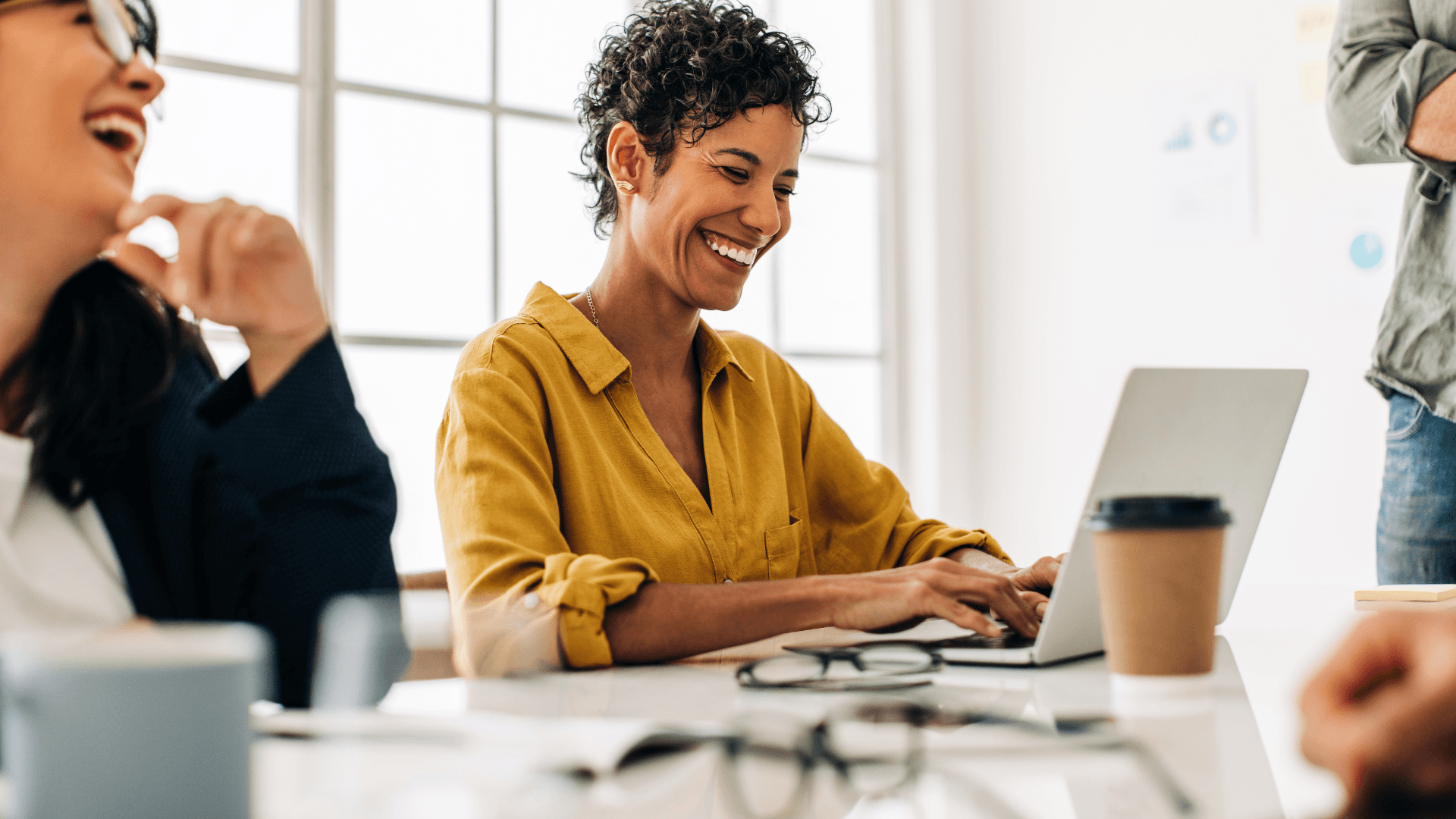 A group of people in an office sitting at a table, gathered around a laptop.